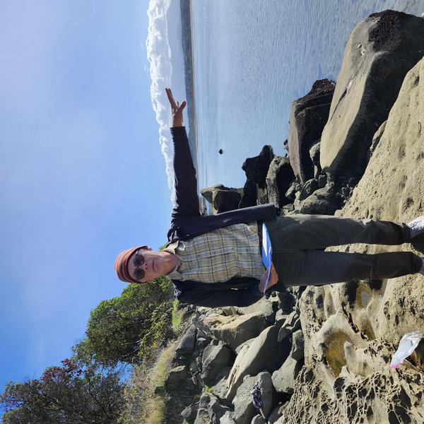 Alan Gilchrist lecturing on a rocky outcrop on the shore on a sunny day