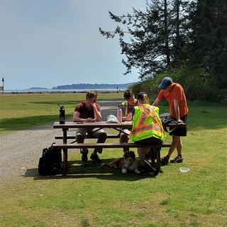 A sunny day at the park with students sitting at a pick nick table taking notes with an instructor helping.