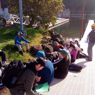 Students sitting along a dock listening to an instructor. A sunny day at a boat launch.
