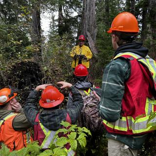 man facing students in heavy brush in the forest speaking